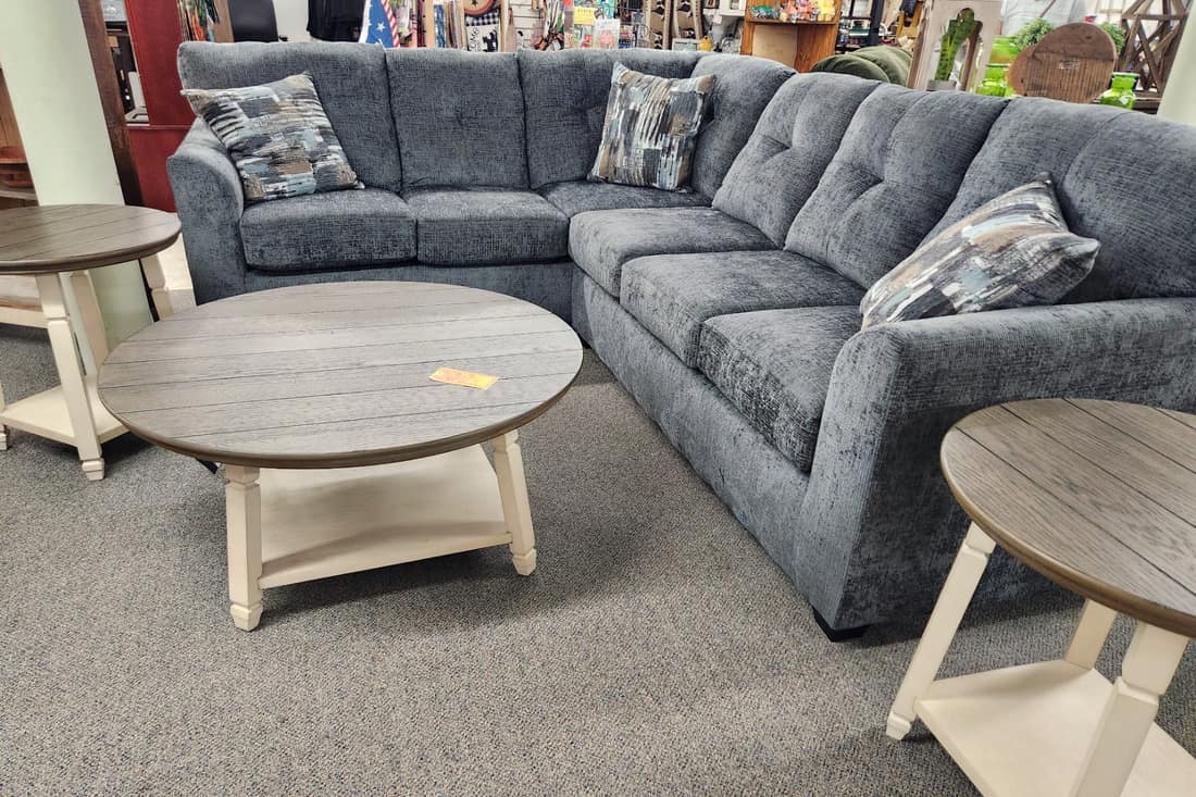 A blue grey tufted corner sectional with a round two tone coffee table on the first floor at Thieves Market